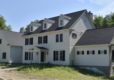 exerior shot of a freshly completed build of a white colonial three floor home with dark roof and shutters.