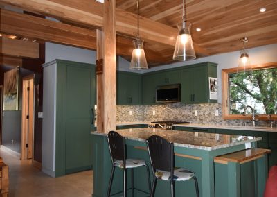 Interior wooden shot of a green and tiled kitchen with several exposed support beams.